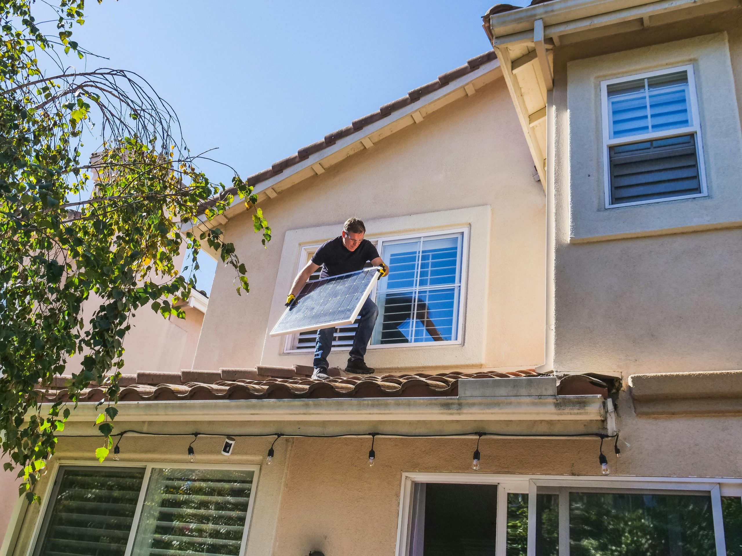 man holding a solar panel, standing on a roof under clear skies
